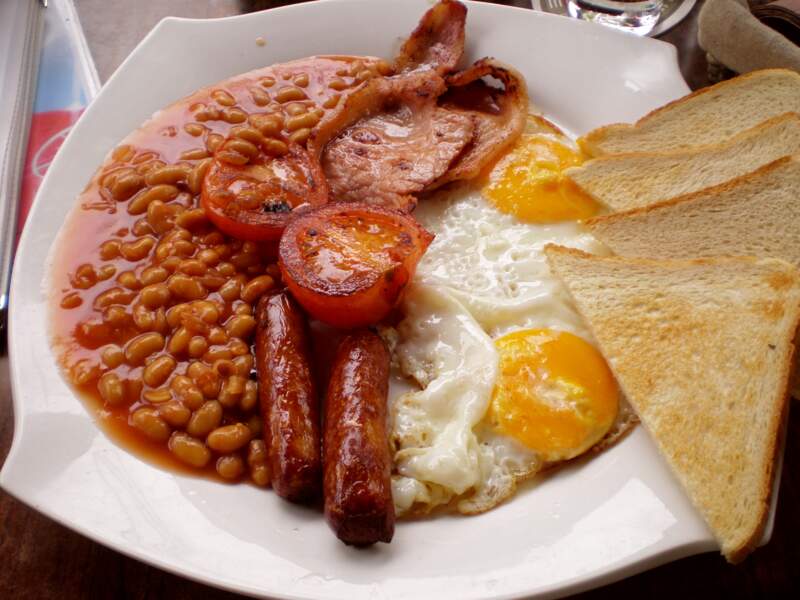 En Angleterre, English breakfast (bacon, œuf au plat, saucisse, toast, tomates et champignons frits).